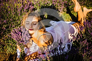 Beautiful model holding a bouquet of fresh lavenders relaxing in the spring or summer lavender field under the rays of the sun.