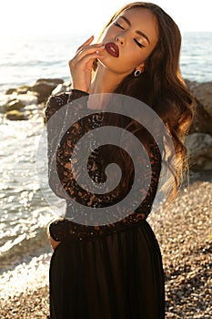 Beautiful model in lace black dress posing on beach