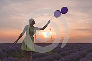 A beautiful model with long braids stands in a lavender field. Holds two balloons in his hands. Sunset in the background