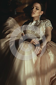 Beautiful model in luxurious puffy dress with veiling skirt sitting relaxed in the armchair