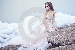 Beautiful model in luxurious strapless corset ball gown sitting on slabs of broken ice at the misty seaside