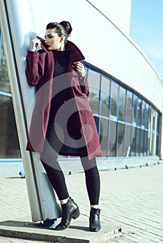 Beautiful model with perfect make up and hair scrapped back into a bun leaning on the column of modern building
