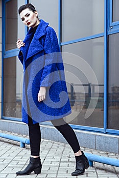 Beautiful model with perfect make up and hair scrapped back into a bun walking in trendy blue coat