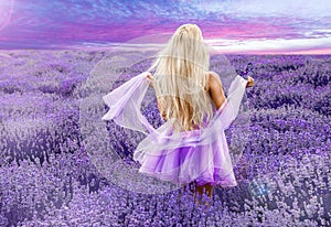 Beautiful model walking in spring or summer lavender field in sunrise . Blond long haired girl in lavender field