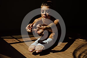 Beautiful modern ballet dancer with perfect body sits on the floor in the studio hall.