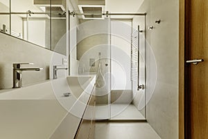 Beautiful modern bathroom with gray stone-like tiles, large mirror integrated into the wall, heated towel rail and chrome in the