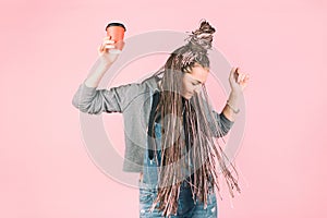 Beautiful modern fashionable girl with pink zizi afro-braids dancing with a cup of coffee in her hands on a pink background