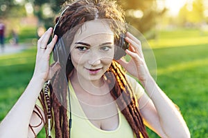 Beautiful modern girl with dreadlocks listening to music with headphones in autumn Sunny Park. Melomania and good mood