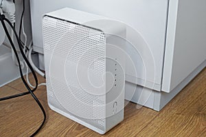 A beautiful modern white home wifi router is connected and stands on the floor in a home room.