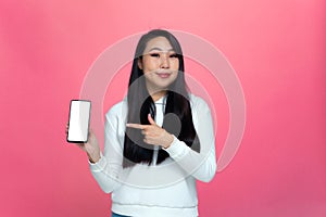 Beautiful modern young asian girl showing smartphone with empty blank white screen for ad, recommending new apps