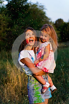 Beautiful mom and daughter play with Hol colors. multi-colored paint on clothes and face photo