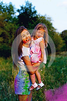 Beautiful mom and daughter play with Hol colors. multi-colored paint on clothes and face