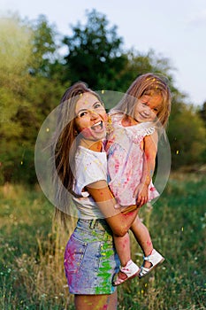 Beautiful mom and daughter play with Hol colors. multi-colored paint on clothes and face photo