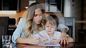 Beautiful mom helps her son to paint with colored pencils image. Helping to develop a child`s imagination.