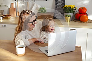 Beautiful mom working at home on a laptop computer while taking care of her baby girl