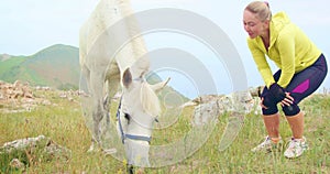 Beautiful moment human and animal. The woman sits, relax and looks at beautiful white horse. Love for pets. Mountain