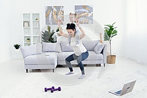 Beautiful mommy and charming little daughter are smiling while doing fitness exercises together at home.