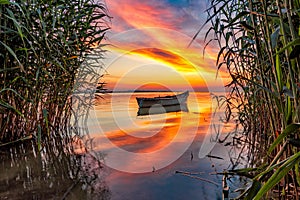 Beautiful morning landscape with a boat on the lake at the sunrise through the reed