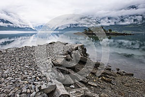 Beautiful morning landscape on fjord. Stone pier and rocky island with trees and creeping clouds, Norway