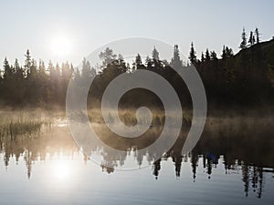 Beautiful morning orange sunrise over lake Sjabatjakjaure with haze mist in Sweden Lapland nature. Mountains, birch trees, spruce