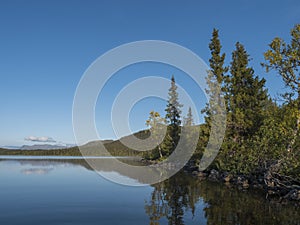 Beautiful morning over lake Sjabatjakjaure in Sweden Lapland nature. Mountains, birch trees, spruce forest, rock boulders and