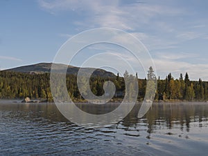 Beautiful morning over lake Sjabatjakjaure with view on Parte Fjallstuga STF mountain cabin, green hills and birch trees. Sweden