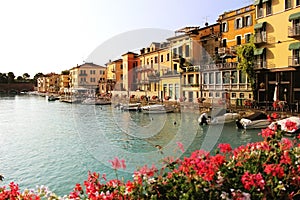 Beautiful morning in Peschiera del Garda town. Colorful houses, architecture view with boats and blurred geranium