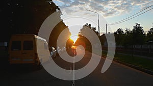 Beautiful morning sunrise in the city street in distant road on the horizon. Cars are parked at the edge of the roadway