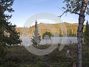 Beautiful morning sunrise over lake Sjabatjakjaure with haze mist in Sweden Lapland nature. Mountains, birch trees, spruce forest