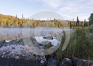 Beautiful morning sunrise over lake Sjabatjakjaure with haze mist in Sweden Lapland nature. Mountains, birch trees, spruce forest