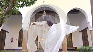 Beautiful Moroccan Girl Spinning and Waving her white mantle in Picturesque Dar Si Said Riyad in Marrakech at sunset