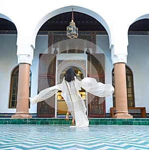 Beautiful Moroccan Girl Waving her white mantle in Rich interior of Picturesque Dar Si Said Riyad in Marrakech