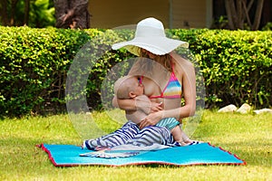 Beautiful mother breastfeeding child in the open air. Nature. Outdoor portrait of a happy family. The joy. The baby and mother in