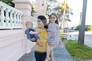 Beautiful mother carrying her happy young daughters in peaceful neighborhood