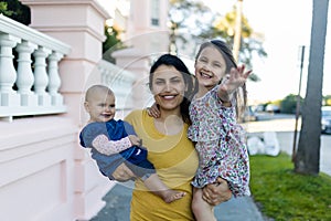 Beautiful mother carrying her happy young daughters in peaceful neighborhood