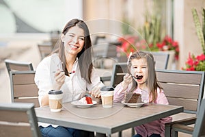 Beautiful mother and daughter having cake at cafe