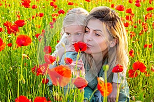 Beautiful mother and daughter in spring poppy flower field. Mom holds her child daughter in the flowering meadow. Spring