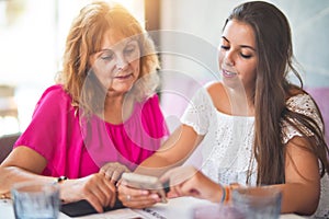 Beautiful mother and daugther sitting at restaurant using smartphone smiling