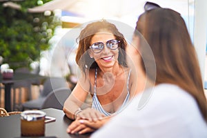 Beautiful mother and daugther sitting at terrace of a restaurant speaking and smiling