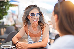 Beautiful mother and daugther sitting at terrace of a restaurant speaking and smiling