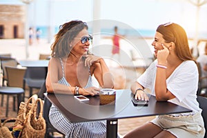 Beautiful mother and daugther sitting at terrace of a restaurant speaking and smiling