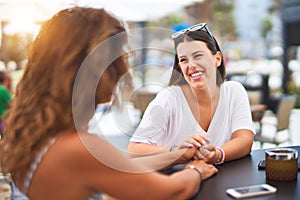 Beautiful mother and daugther sitting at terrace of a restaurant speaking and smiling