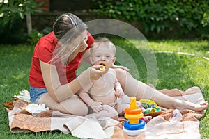 Beautiful mother feeding her baby boy on grass at park