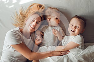 Beautiful mother having fun with her sons in bed in the morning