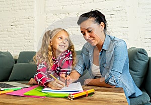 Beautiful mother helping her young blonde cute sweet girl to do homework at home in homework parenting and education concept