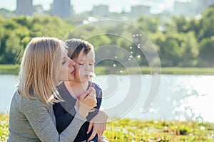 Beautiful mother and her cute baby son blowing blow away a dandelion balloon in the park on a background of green grass