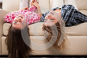 Beautiful mother with her cute daughter lying on the couch with their head upside down