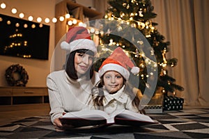Beautiful mother and her cute little daughter in warm knitted white sweaters reading fairy tale book