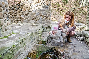 Beautiful mother with her daughter Baby drink water from the holy spring that flows from the rock among the vegetation