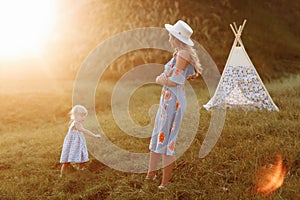 Beautiful mother with her little daughter having fun near wigwam in the field. Spending time together  outside  on vacation